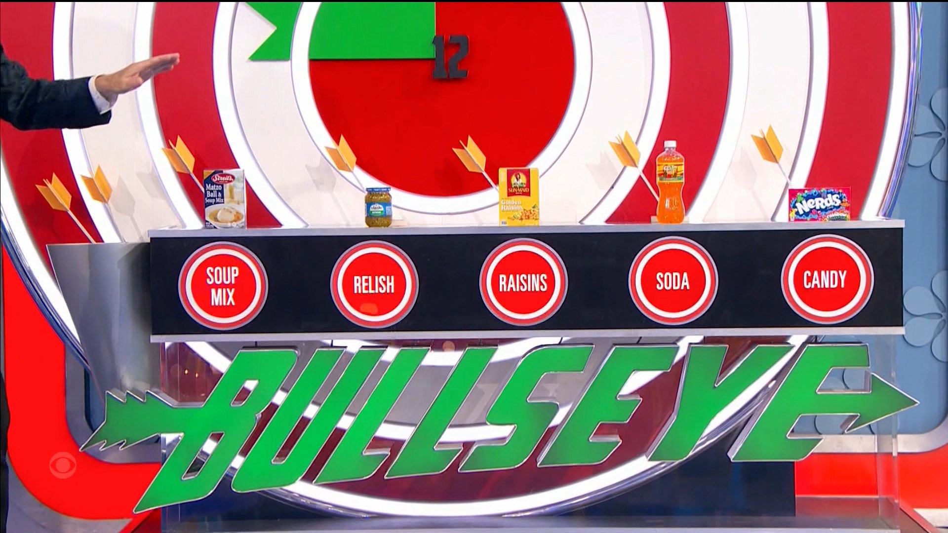 A game setup for 'Bullseye' featuring five grocery products: soup mix, relish, raisins, soda, and candy, with a bullseye target in the background.
