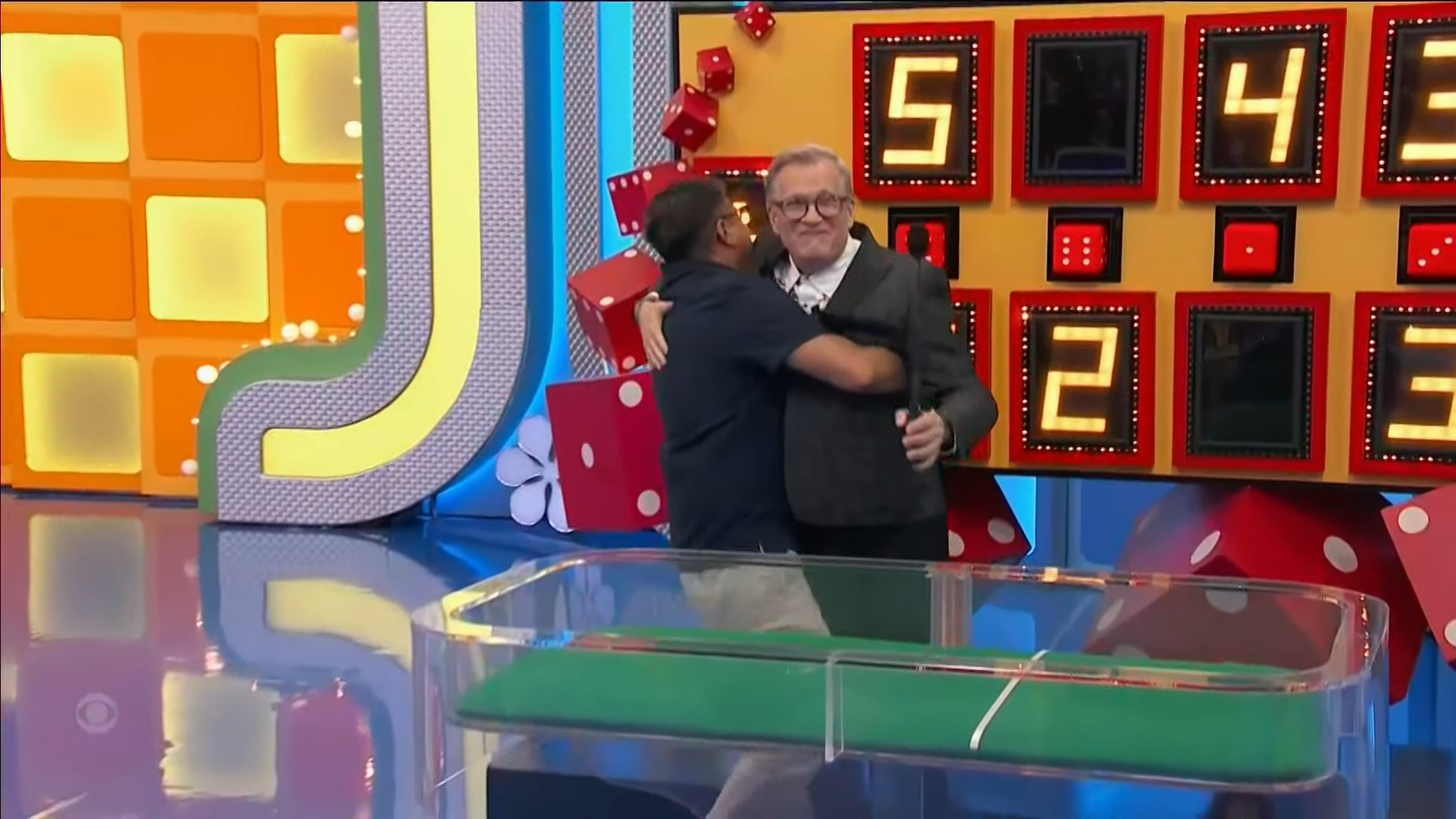 A contestant joyfully embraces the host of the Dice Game in front of a colorful game board featuring oversized dice and illuminated numbers.