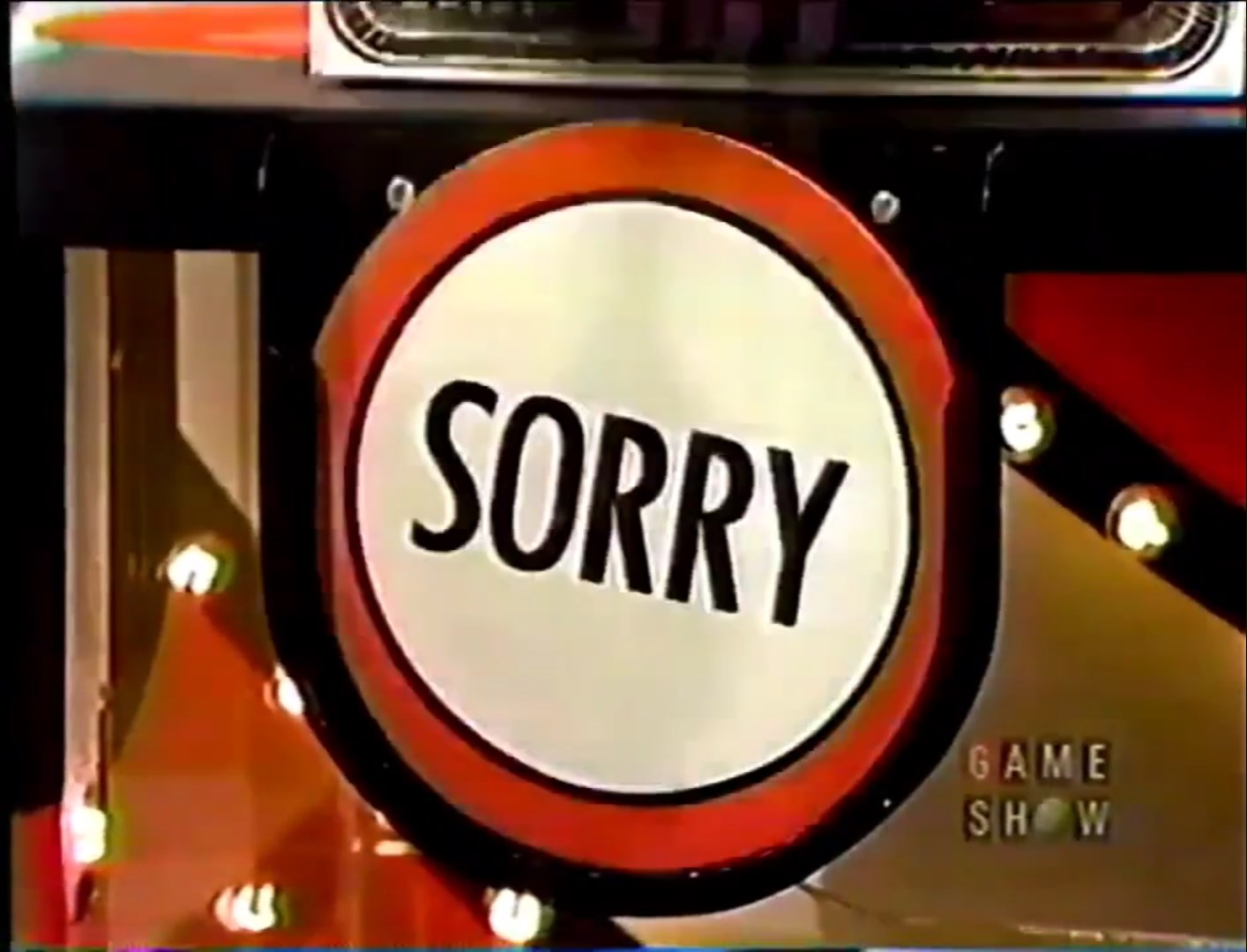 A circular sign with the word 'SORRY' prominently displayed in bold letters, set against a red border, with game show lights in the background.