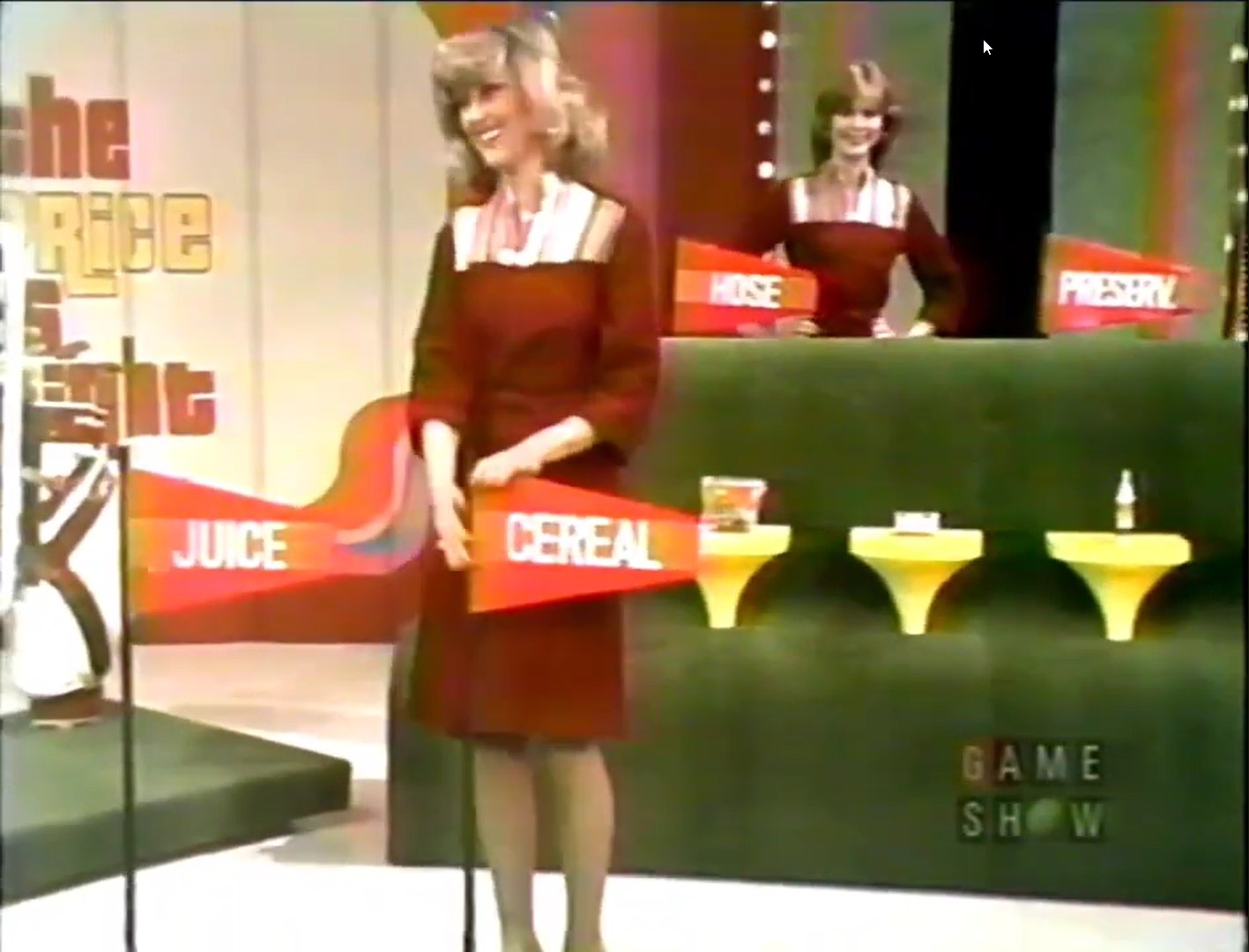 Two contestants holding signs for grocery items 'Juice' and 'Cereal' on The Price is Right set, with a display of additional products in the background.