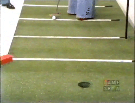 A close-up view of a putting green with lines and a hole, featuring a golf ball in motion towards the hole.