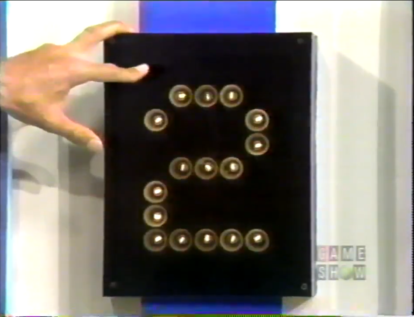 A hand points to the number '2' displayed on a game show board, surrounded by light bulbs.