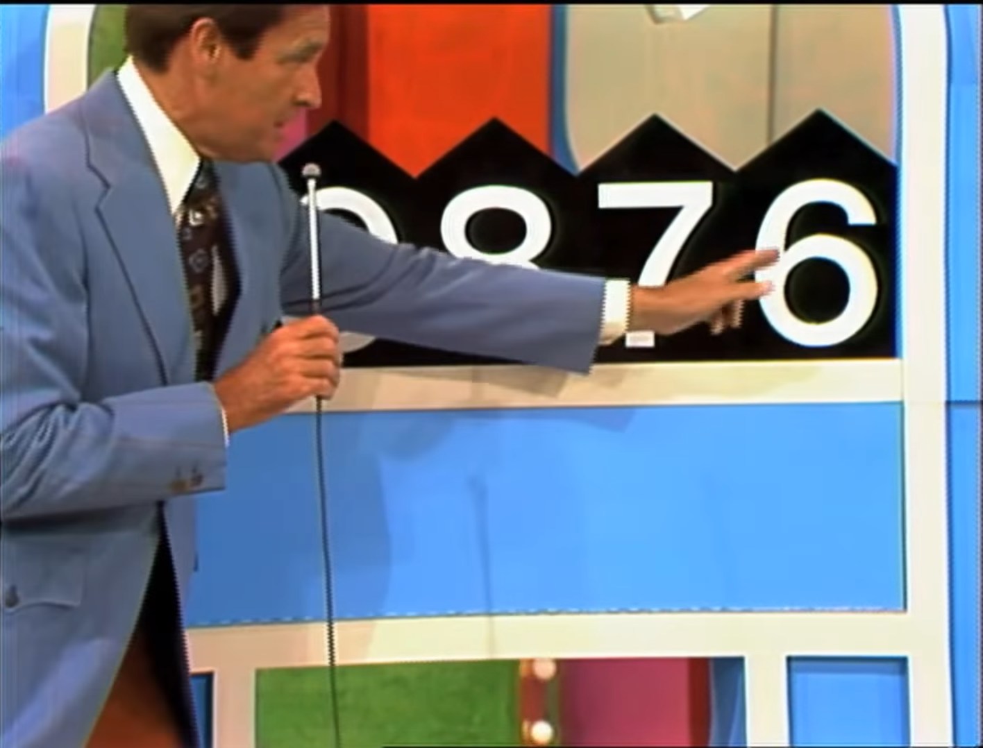 Host pointing to the game board displaying the numbers 0, 9, 7, 6 for the Squeeze Play game.