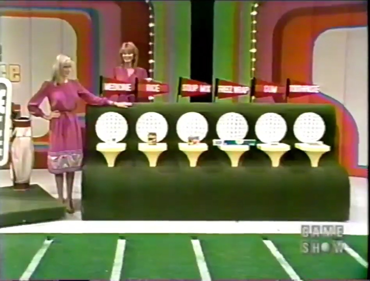Models stand near a putting green featuring grocery products with flags labeled by price.