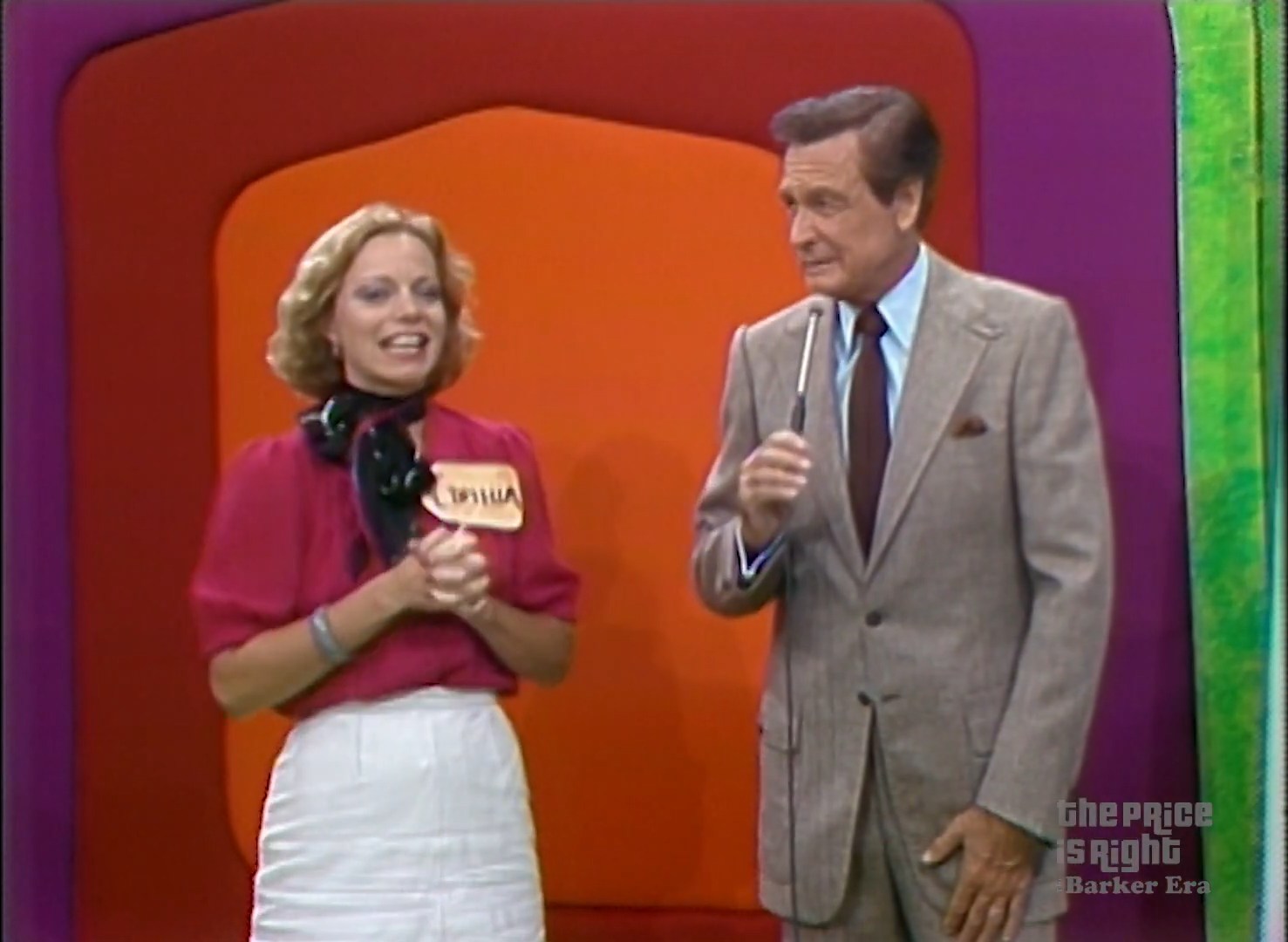 A contestant smiles while standing with a host on the set of The Price is Right game show, with colorful backgrounds.