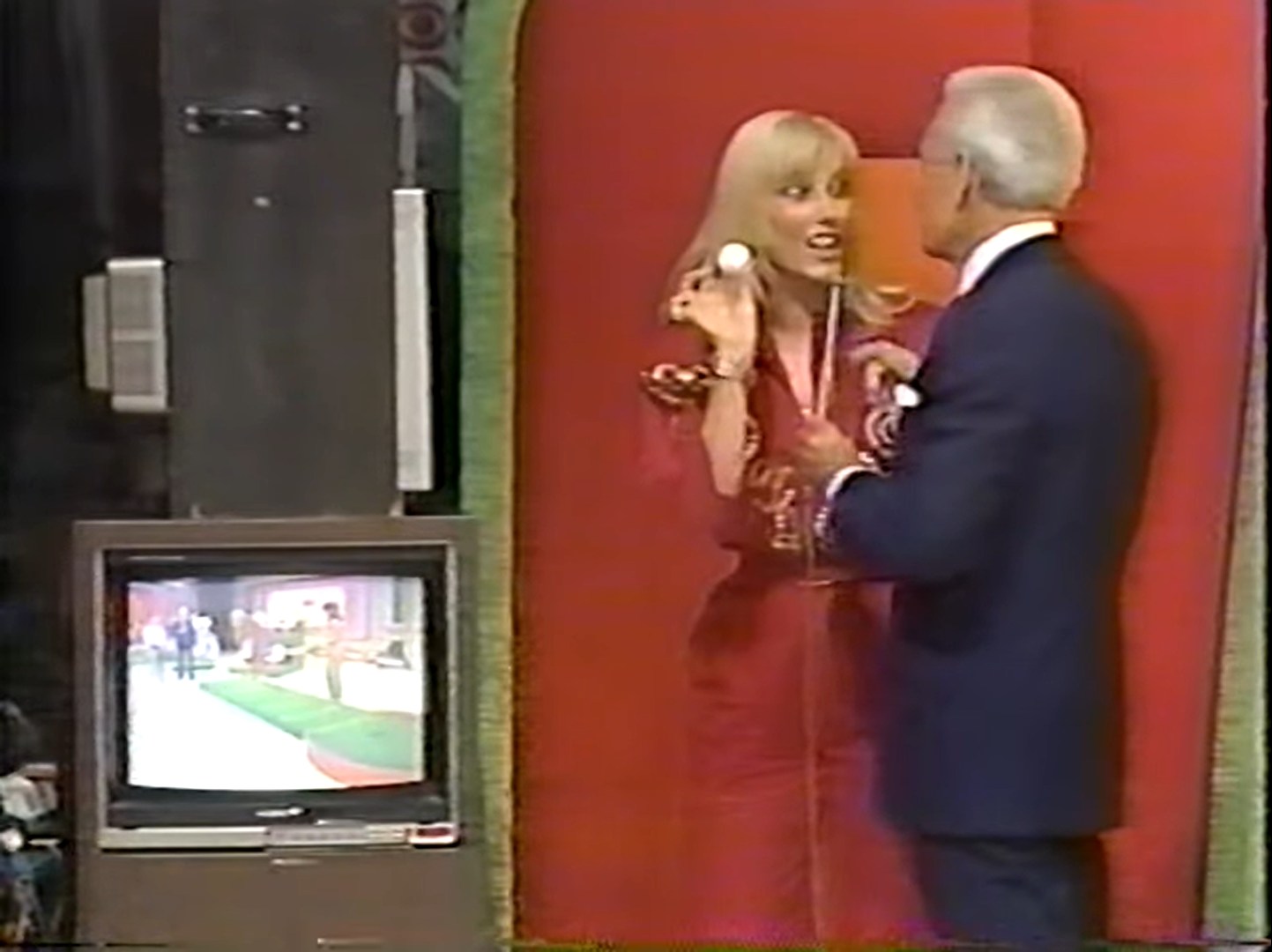 Janice Pennington and Bob Barker interact on stage, with Janice holding a golf ball while looking excited, and a television in the background displaying a putting green and other contestants.