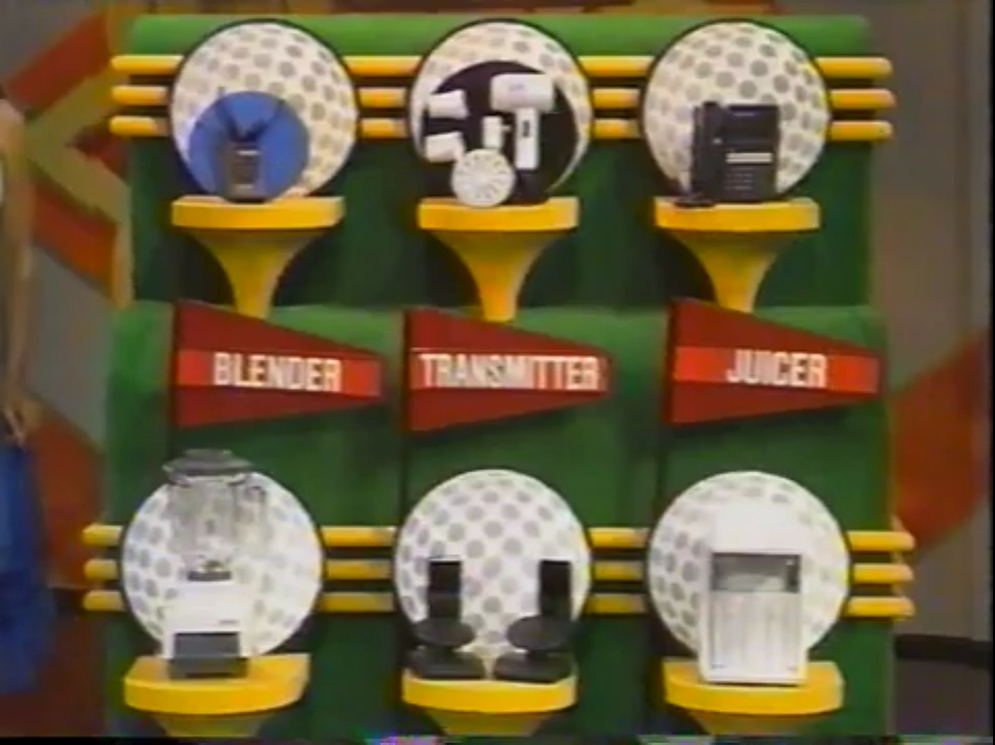 Display of six grocery products labeled 'Blender,' 'Transmitter,' and 'Juicer' on a game show set with a putting green backdrop.