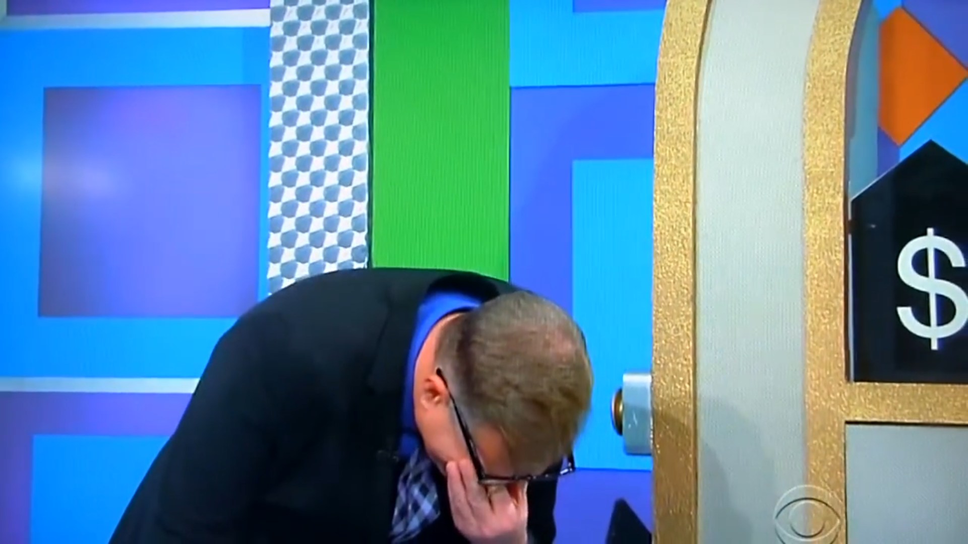 Drew Carey stands with his hand on his forehead, appearing frustrated, in front of a colorful game board.