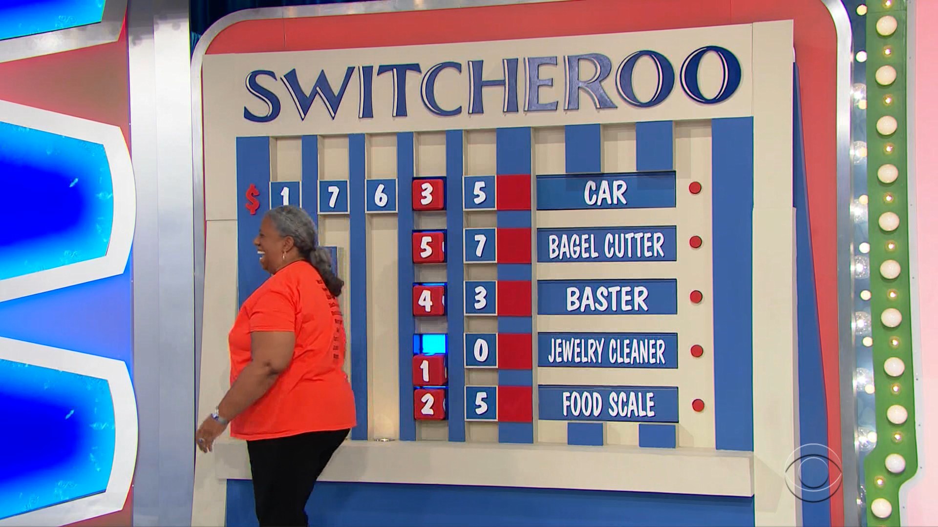 A contestant playing the game 'Switcheroo' on The Price is Right, standing next to a game board displaying missing price digits for prizes including a car, bagel cutter, baster, jewelry cleaner, and food scale.