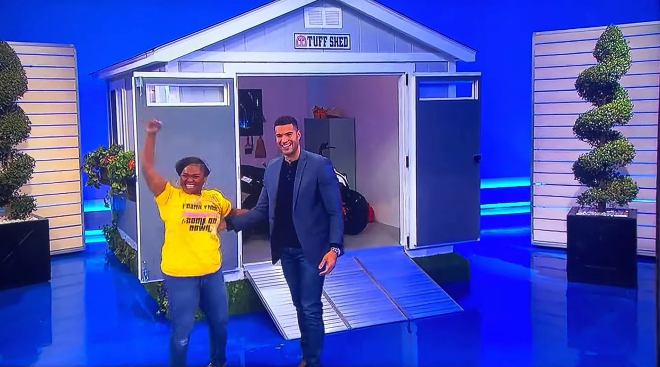A contestant celebrating a win in front of a Tuff Shed on a game show set, with a host smiling beside her.
