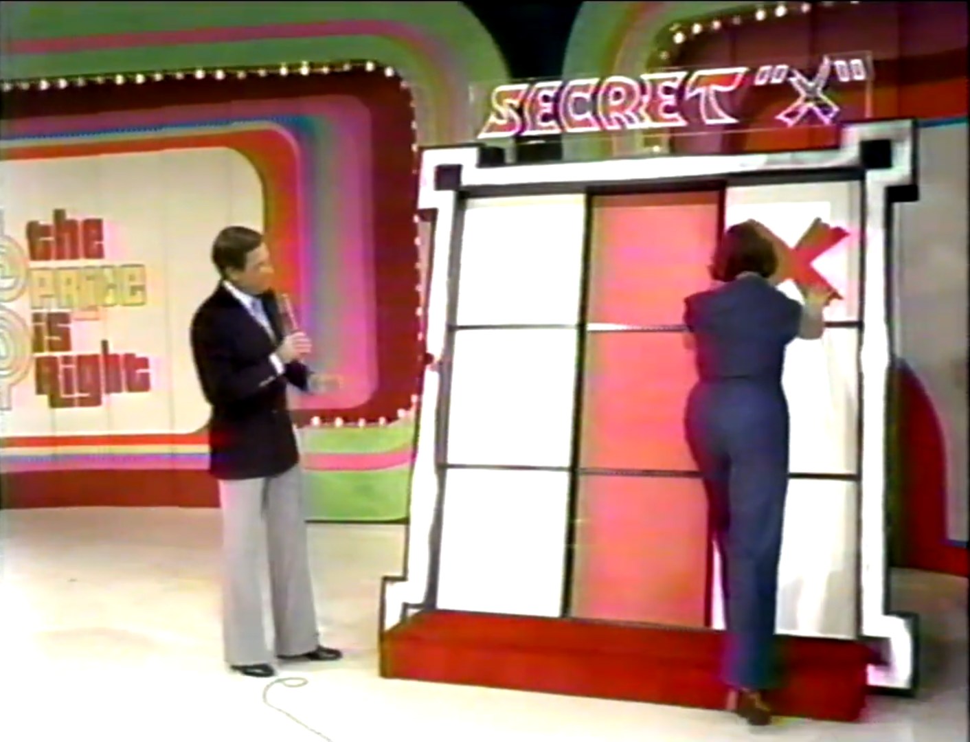 A contestant places an 'X' on a Tic-Tac-Toe board during the Secret 'X' game on The Price is Right, with the host looking on.