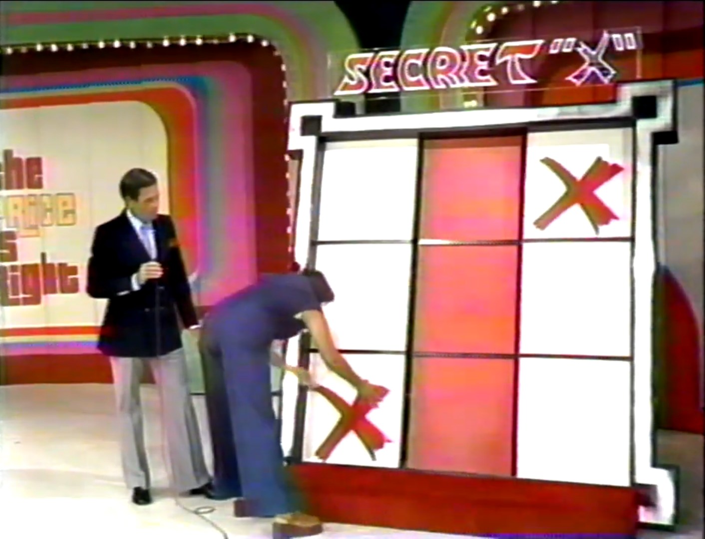 A contestant places an 'X' on a Tic-Tac-Toe board while the host of The Price is Right looks on.