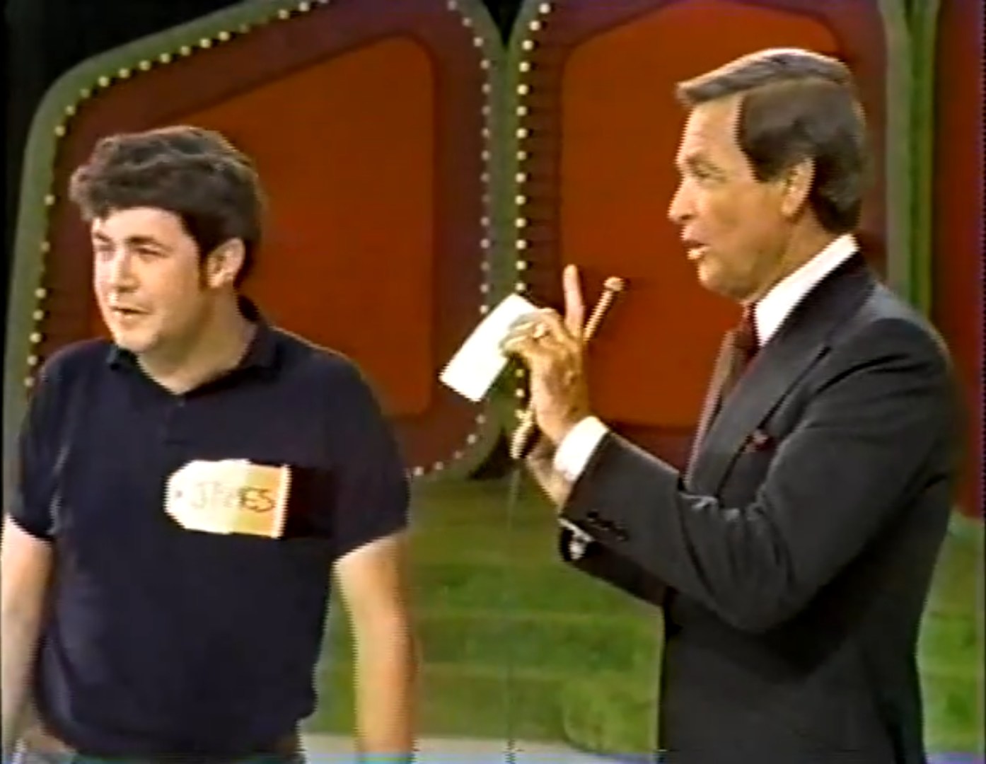 A contestant named James standing on stage during a game on The Price is Right, while the host is holding a microphone and pointing at him.