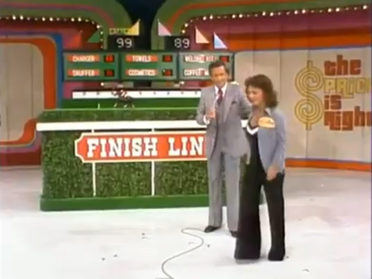 A contestant walks away from the Finish Line game on The Price is Right, with the host beside her, and the scoreboard in the background displaying prices.