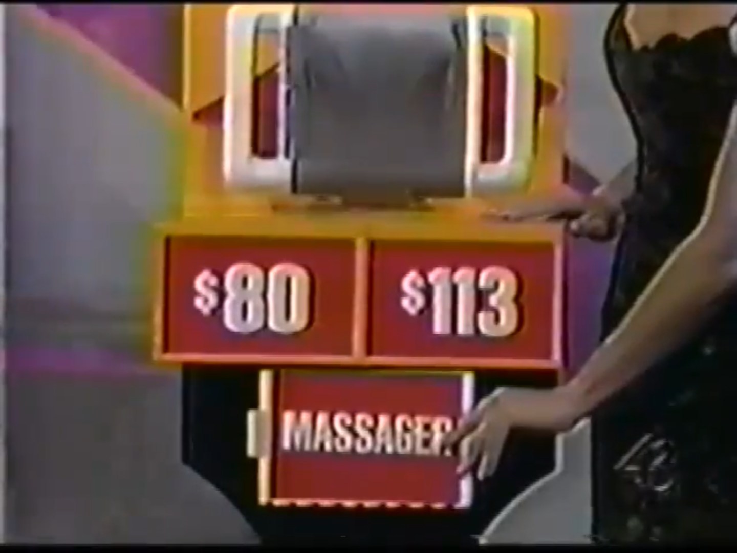 A contestant points to a game board displaying two price options,  and 3, for a massage device.