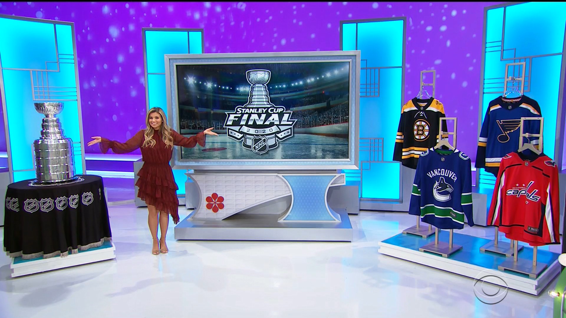 A model stands beside the Stanley Cup on a table, showcasing NHL jerseys from various teams, with a background displaying the Stanley Cup Final logo.