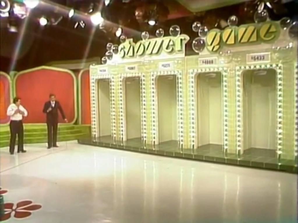 Bob Barker and contestant near a colorful game set labeled 'Shower Game' with six shower stalls in the background.