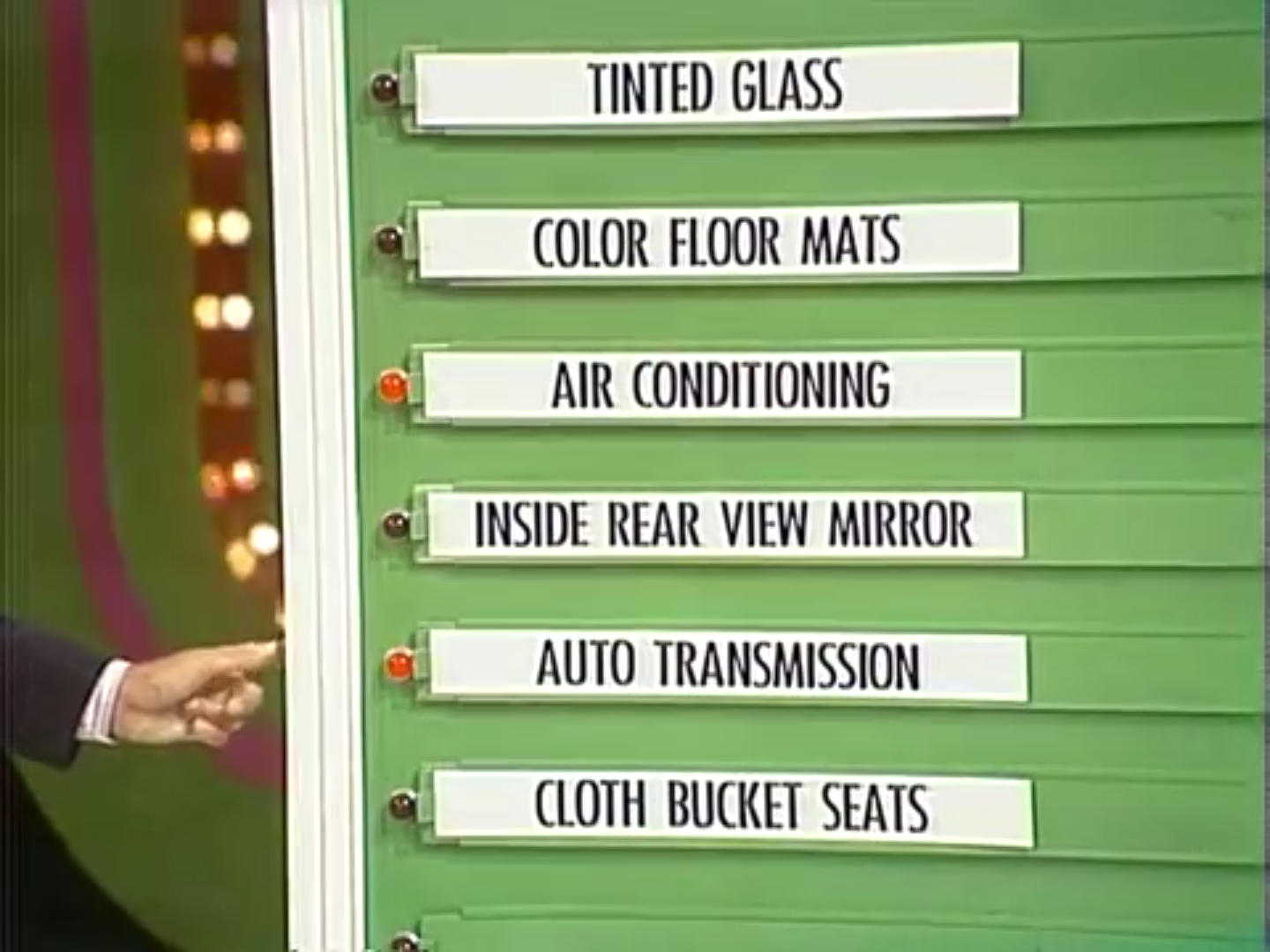 A green board displaying six car options with labels, including 'Tinted Glass,' 'Color Floor Mats,' 'Air Conditioning,' 'Inside Rear View Mirror,' 'Auto Transmission,' and 'Cloth Bucket Seats.'