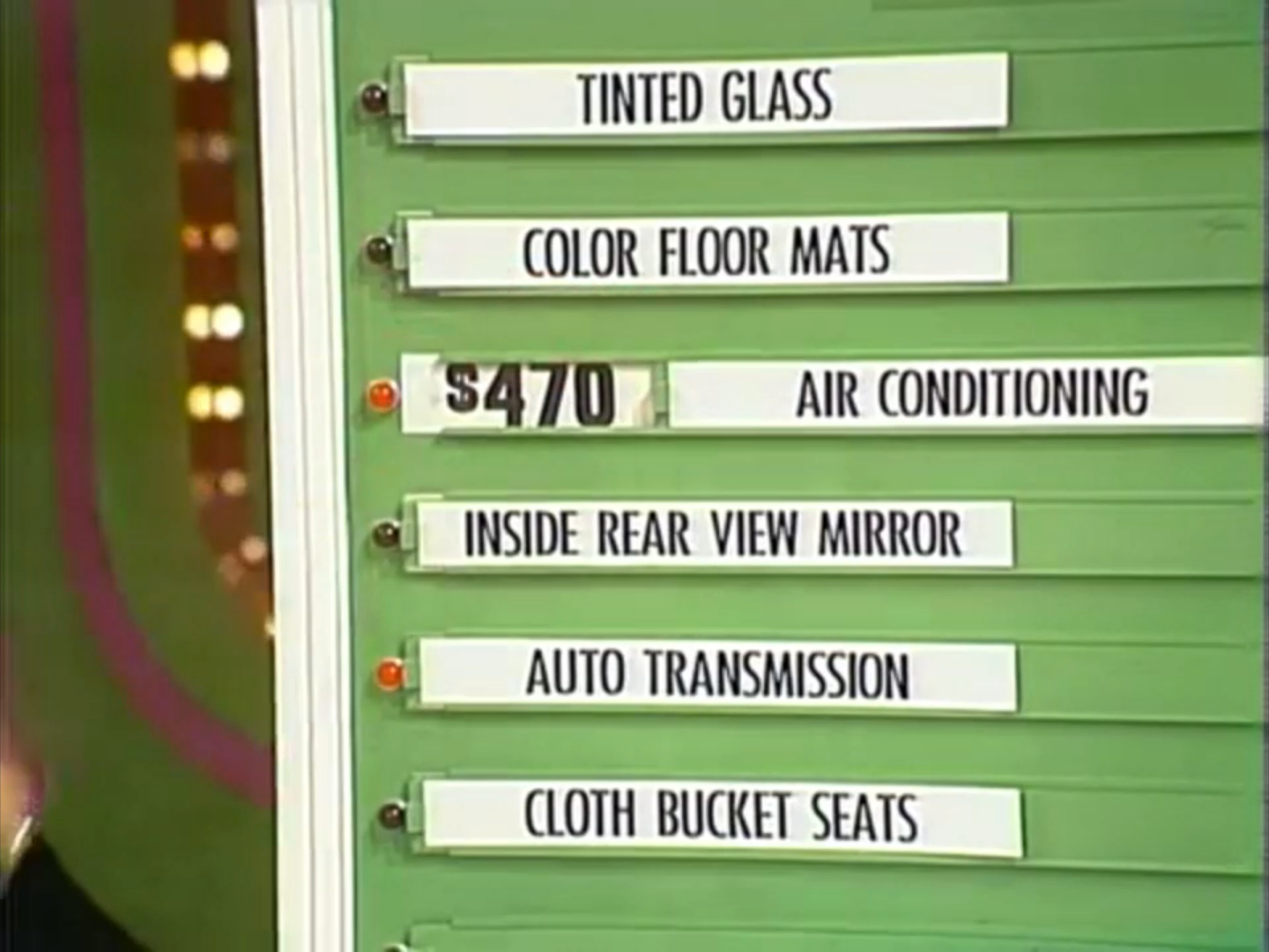 A game board displaying six options for a car contest on The Price is Right, including air conditioning priced at 0, alongside tinted glass, color floor mats, inside rear view mirror, auto transmission, and cloth bucket seats.