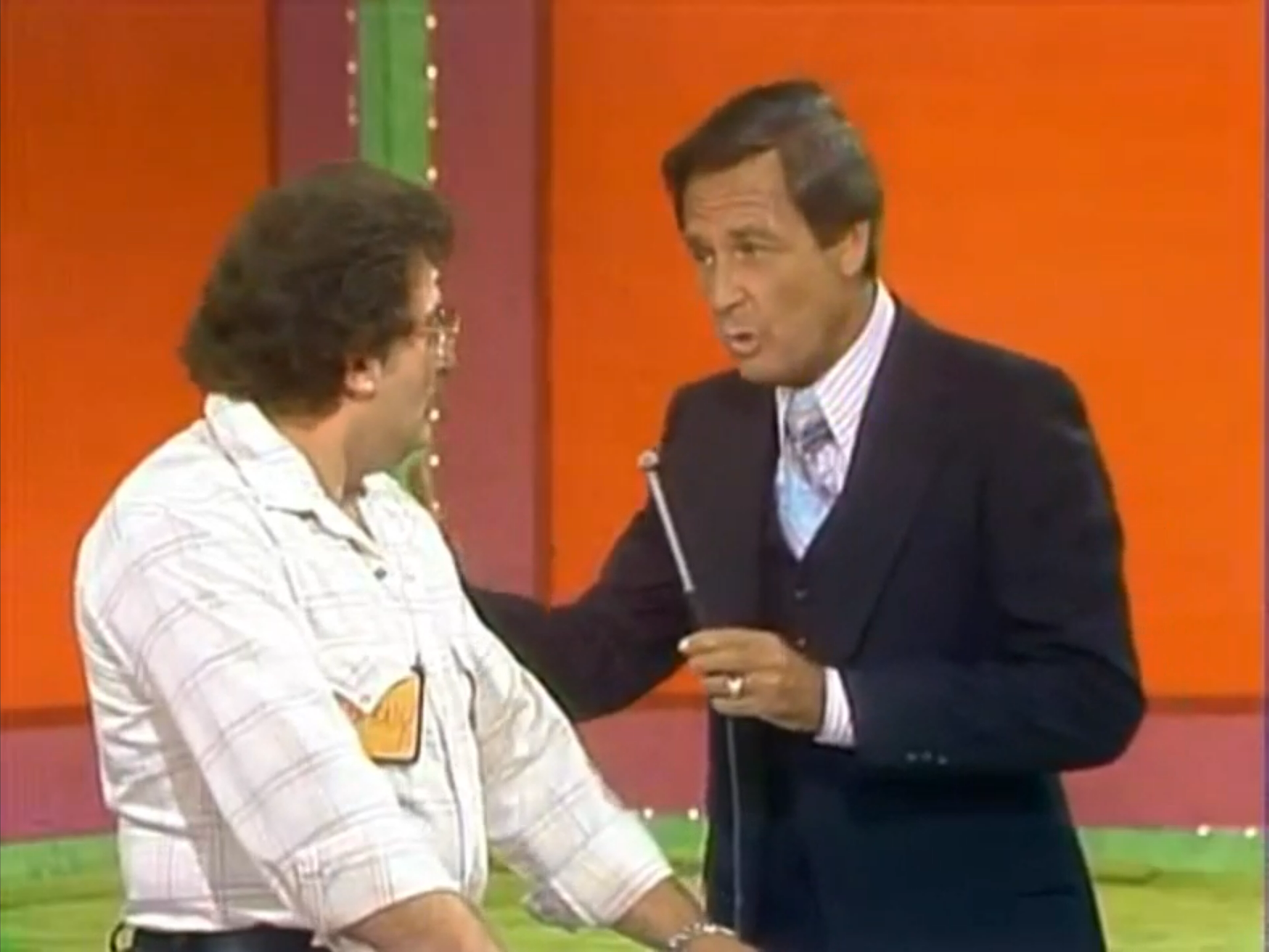 A contestant interacts with the host on stage during the Shower Game segment, with colorful background elements visible.