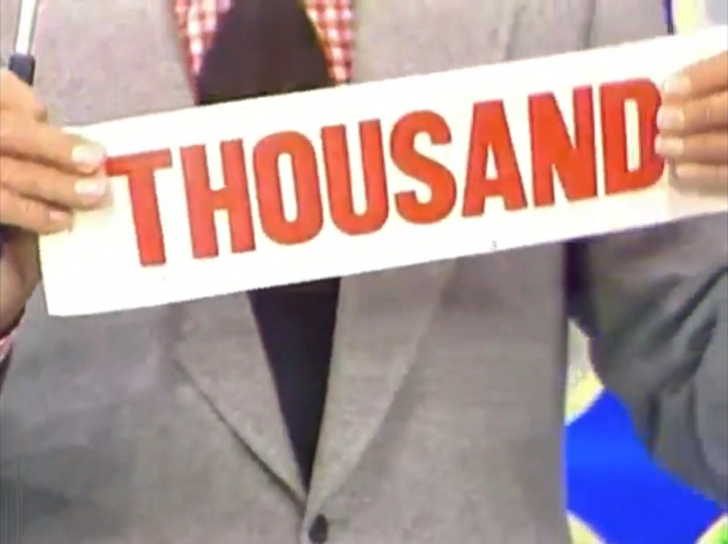 Bob Barker holds up a sign that reads 'THOUSAND' in bold red letters during a game on The Price is Right.