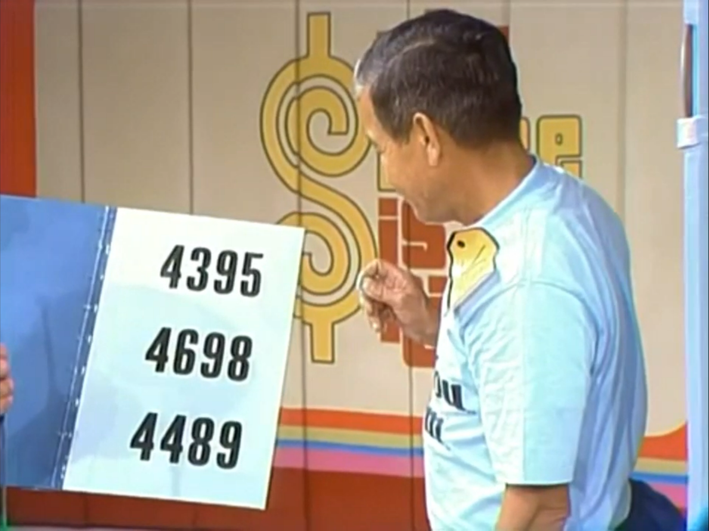 Bob Barker holding a sign with three four-digit numbers, representing prices the contestant can choose in the Telephone Game.