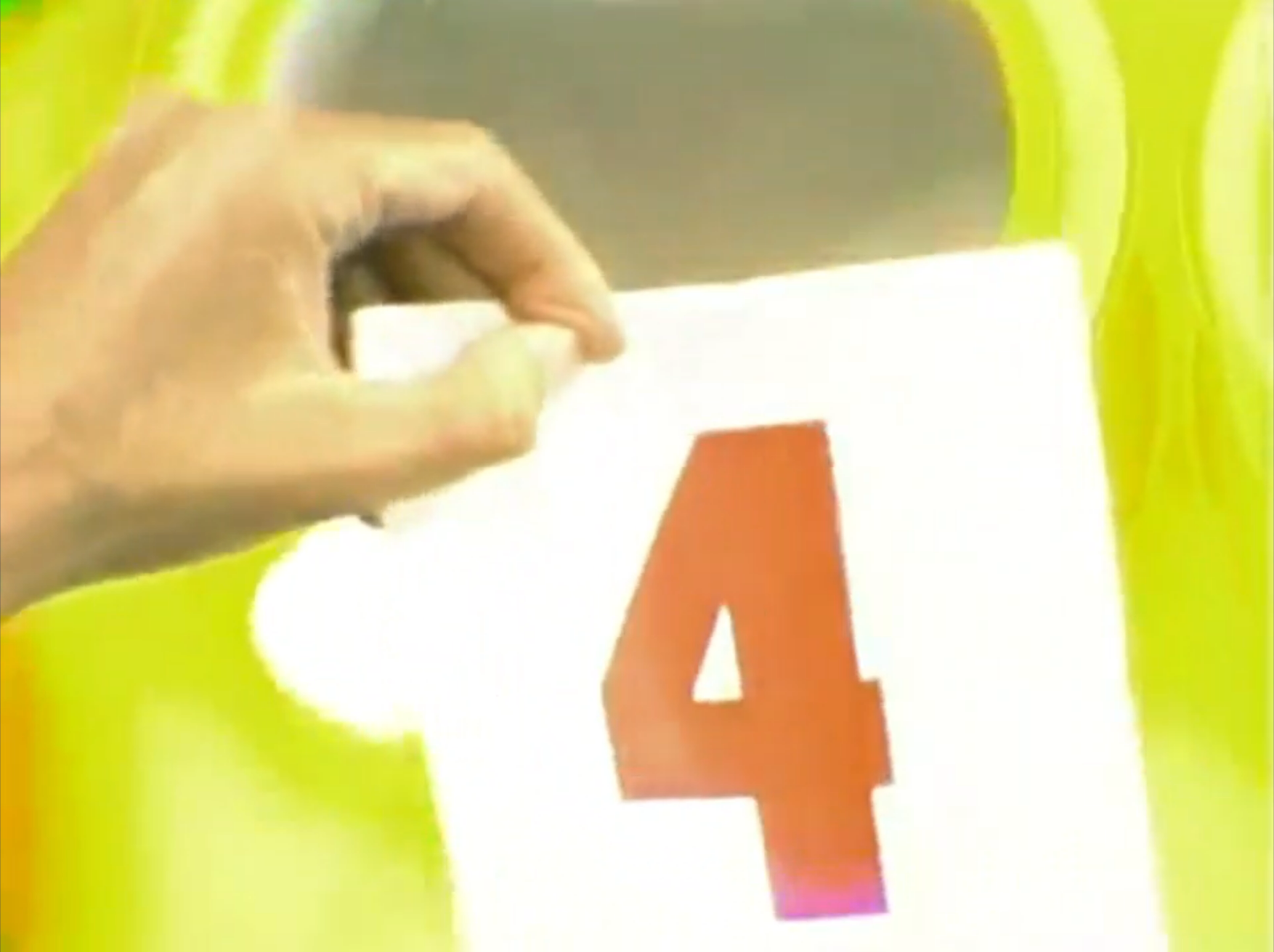 A hand holding a white card with a red number '4', set against a bright yellow background.