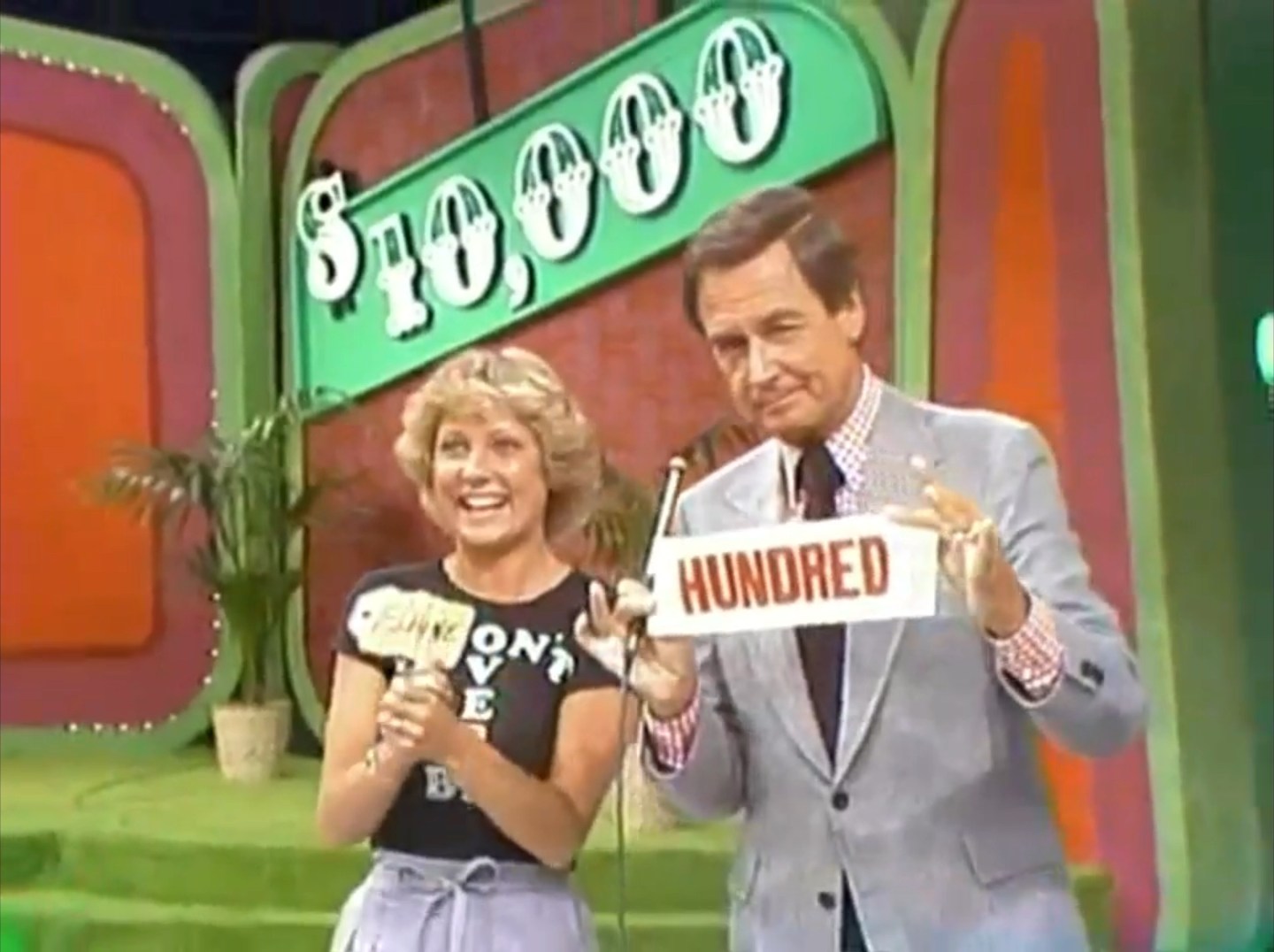 A contestant holding a sign with 'Punch' while smiling, next to a host displaying a 'HUNDRED' sign, with a large ',000' banner in the background.