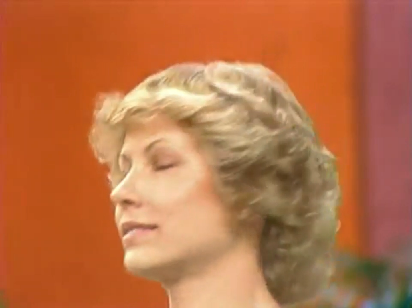 A contestant on The Price is Right with short, curly blonde hair and a focused expression.
