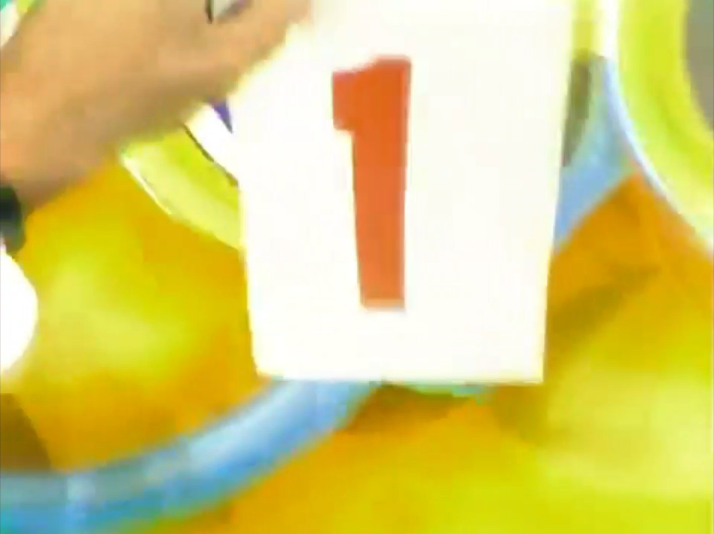 A contestant holding a card displaying the number '1' against a colorful backdrop during a game show.