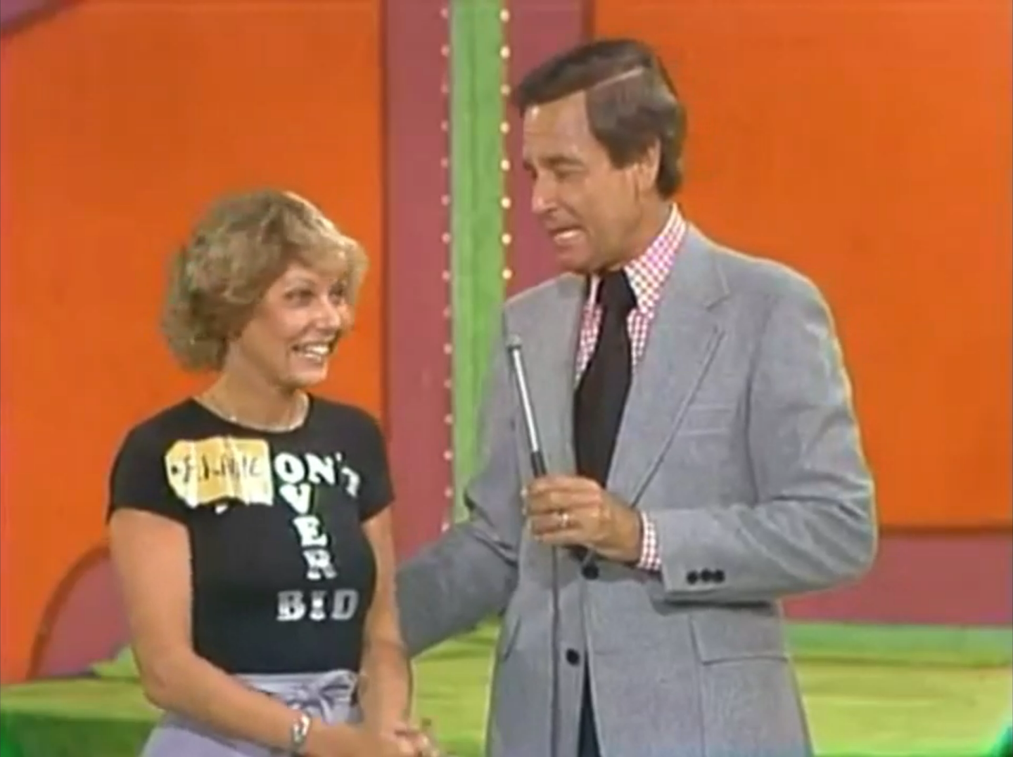 A contestant on The Price is Right smiles as she interacts with the host, wearing a shirt that says 'DON'T OVER BID'.