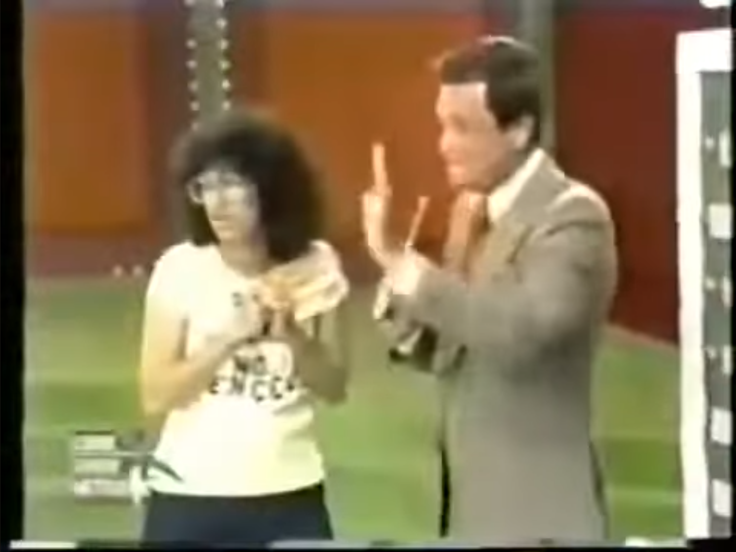 A scene from The Price is Right featuring a female contestant with curly hair holding a prize while Bob Barker gestures with his hands.