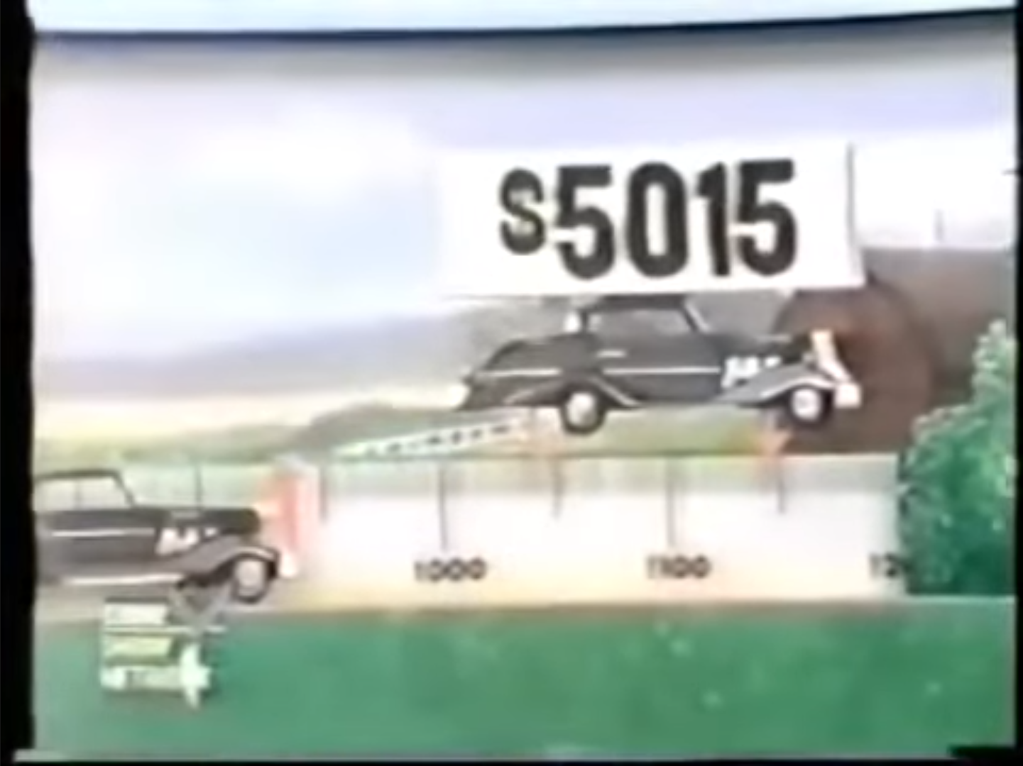 A game show scene from 'The Price is Right' featuring a display of two cars on a ramp, with a price banner showing 15 above them.