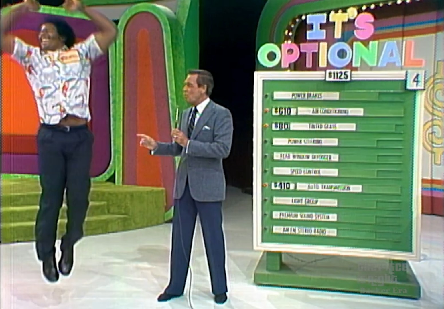 A contestant joyfully leaps in excitement next to the host, who is pointing towards a display board with options and prices for a game called 'It's Optional' on The Price is Right.