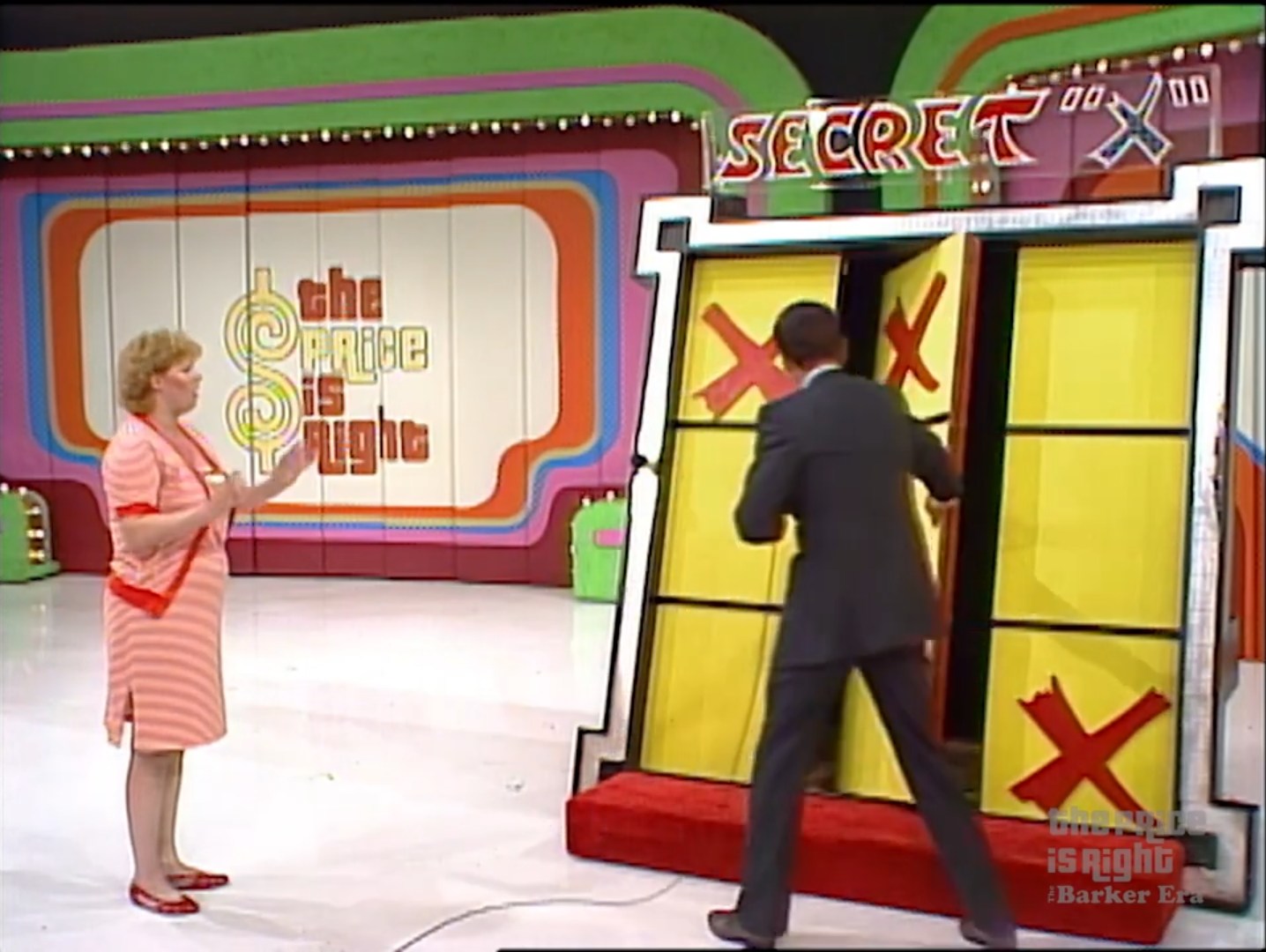 A contestant watches as the game host opens the doors to the Secret 'X' game on The Price is Right, revealing a giant Tic-Tac-Toe board with red 'X's.