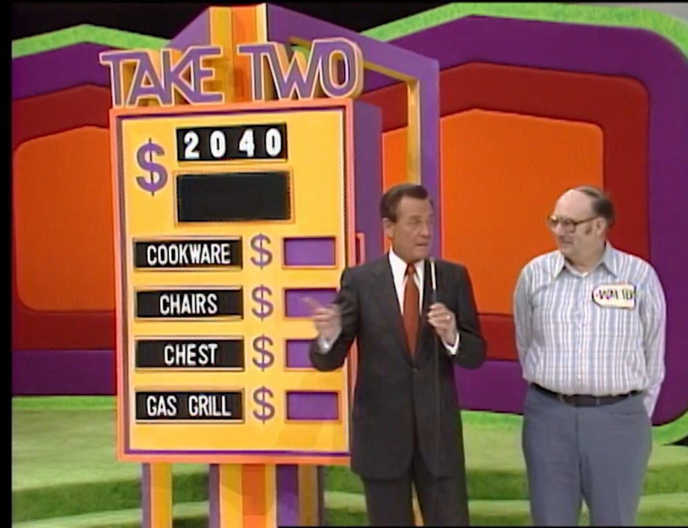A game show host stands next to a contestant beside a game board displaying the title 'TAKE TWO' along with a target price of 40 and four prizes listed: Cookware, Chairs, Chest, and Gas Grill.