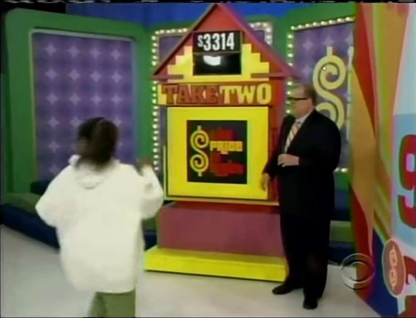 A contestant in a white hoodie turns away from the game board on The Price Is Right's Take Two, while the host stands beside the colorful board displaying a target price of 14.