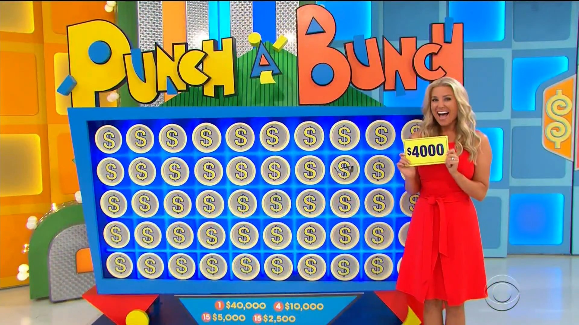 A model in a red dress holds a sign displaying 00 in front of the Punch a Bunch game board, which features various cash prize slips under dollar signs.