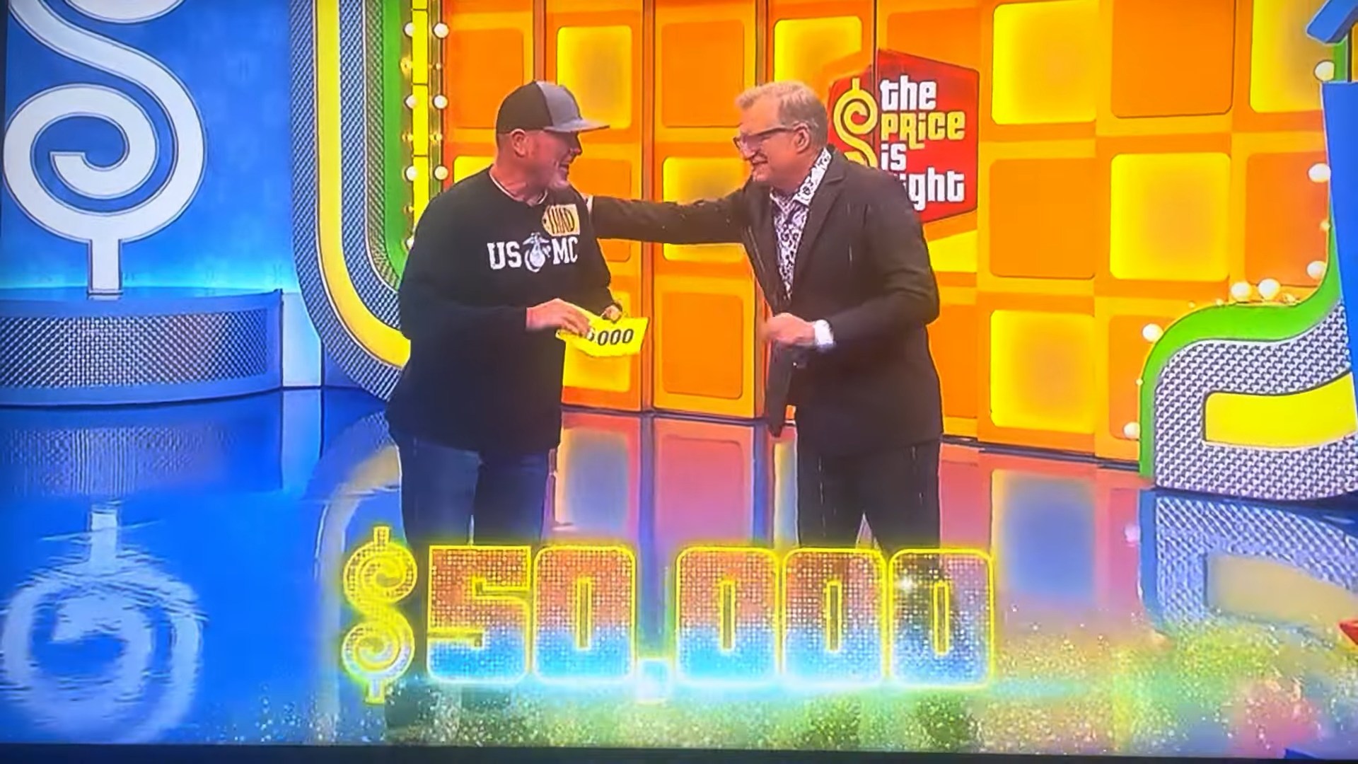 A contestant smiles while holding a sign that reads ,000, celebrating with the host on the set of The Price is Right.