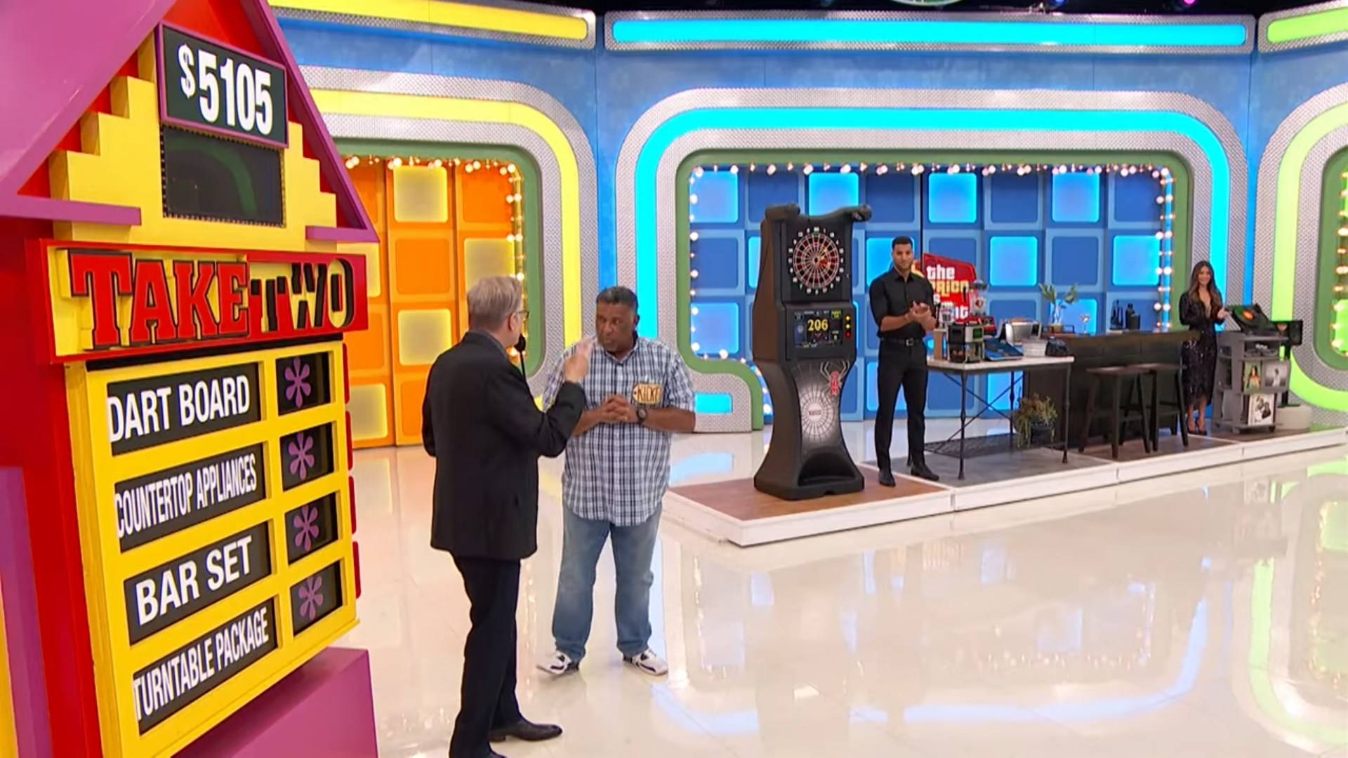 A contestant participates in the game 'Take Two' on The Price is Right, seen discussing with the host while prizes are displayed in the background.