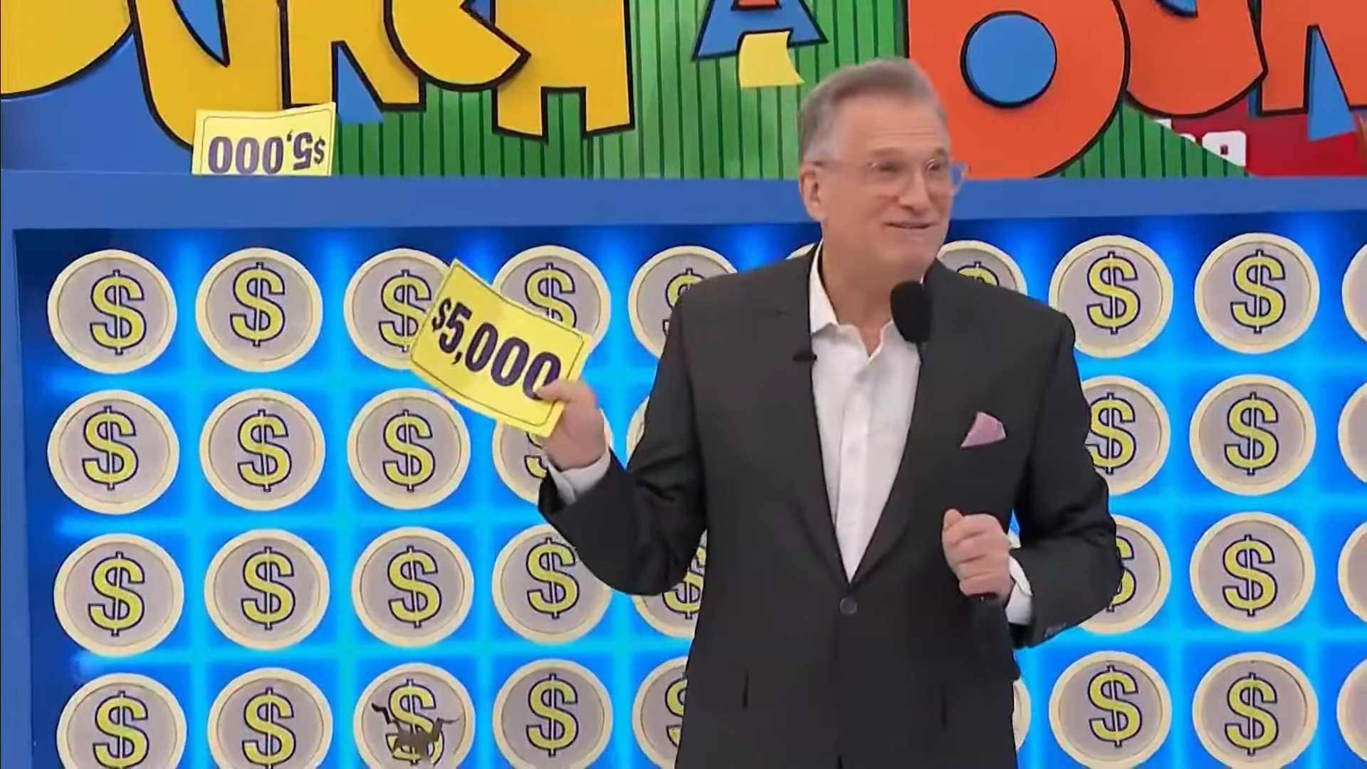 A host from The Price is Right holds up a ,000 prize card in front of a brightly colored punchboard filled with cash amounts.