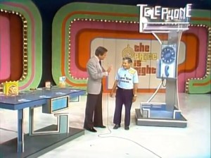 Bob Barker stands next to a contestant in front of a colorful 'Telephone Game' set, with a vintage telephone setup nearby, on the set of The Price is Right.