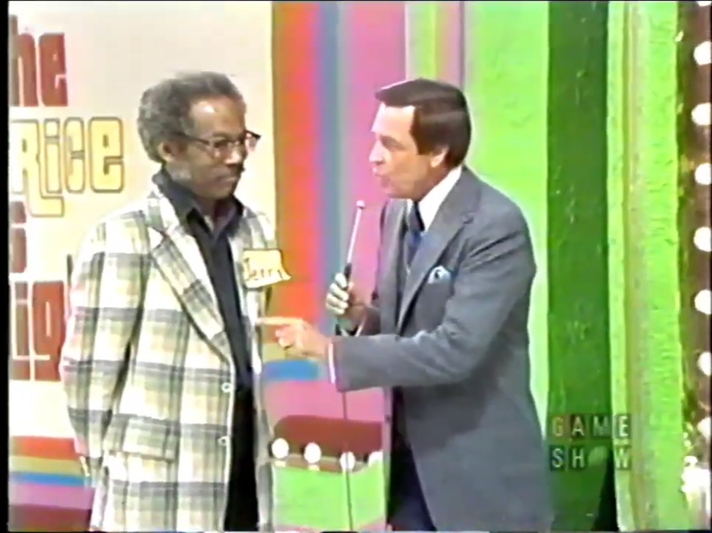 A contestant named Jerry listens as the host explains the game rules on the set of The Price is Right, featuring colorful backgrounds.