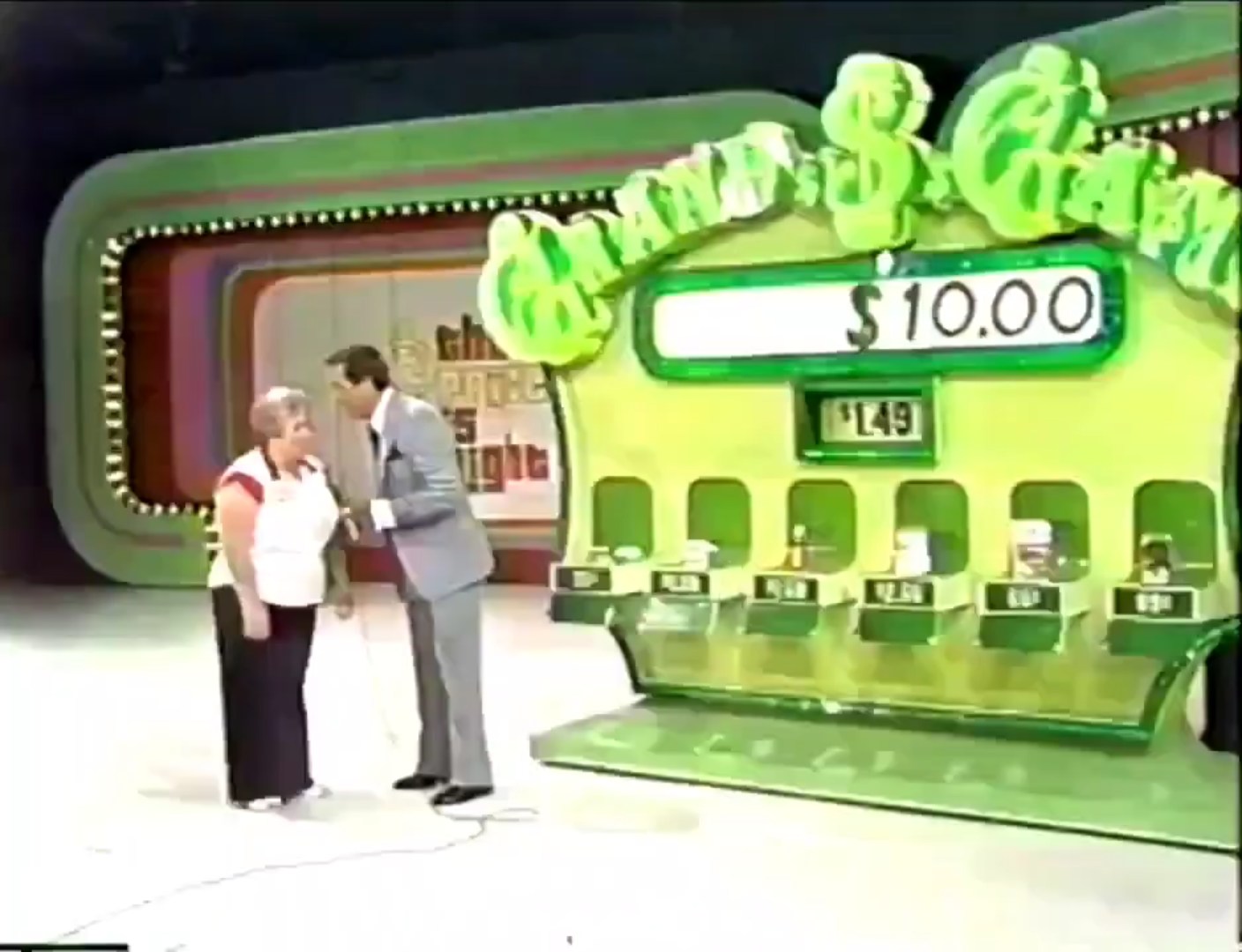Contestant interacts with the host in front of the Grand Game board displaying the initial amount of .00 and six grocery items with their prices.