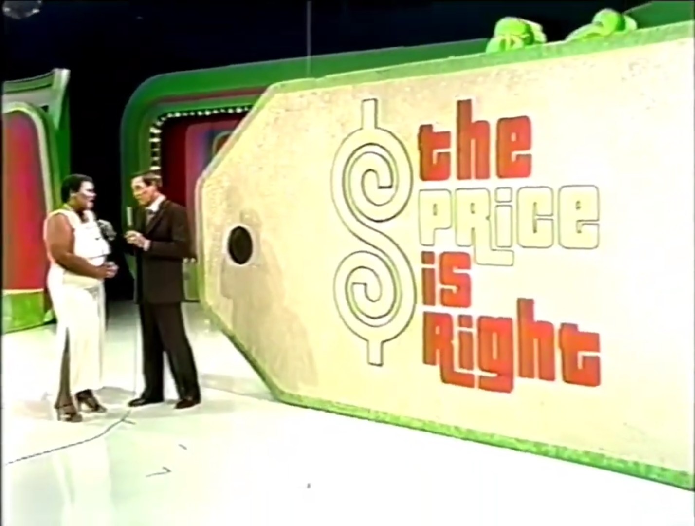 Contestant and host standing next to a large display sign reading 'The Price is Right' on a game show set.