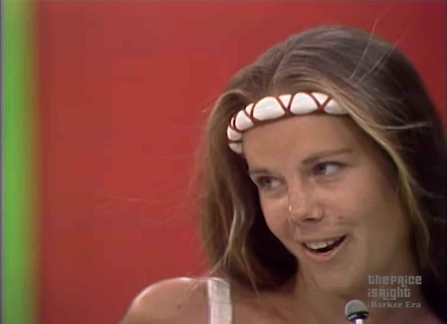 A contestant on The Price is Right smiles while wearing a shell headband against a colorful backdrop.