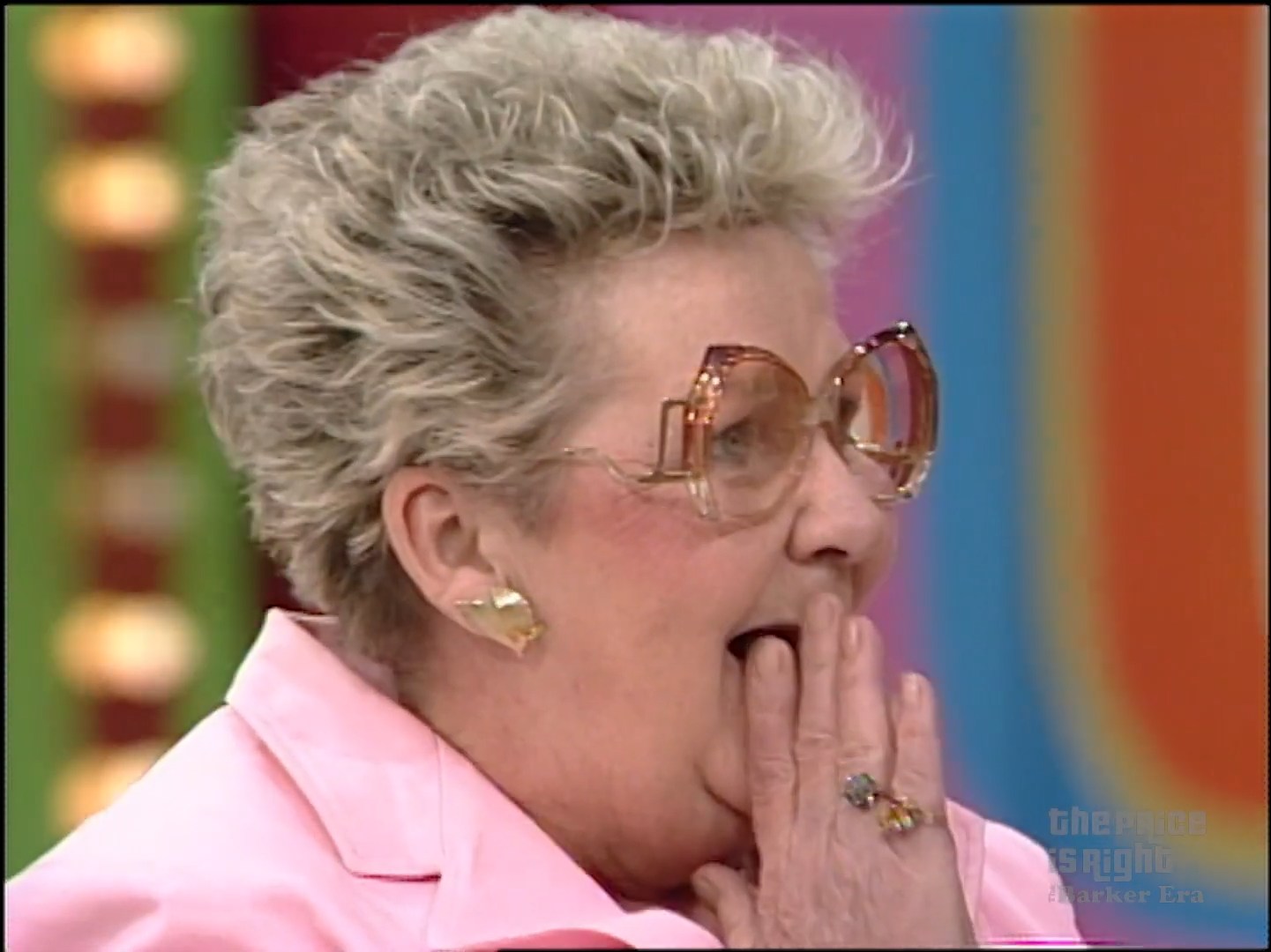 A contestant reacting with surprise and excitement while playing a game on a game show, wearing oversized glasses and a pink outfit.