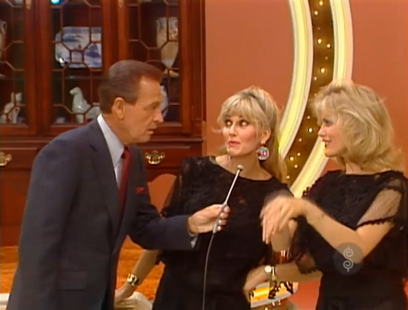 A host interviews two female contestants during the Bargain Game segment on The Price is Right, set against a backdrop of colorful stage decorations.