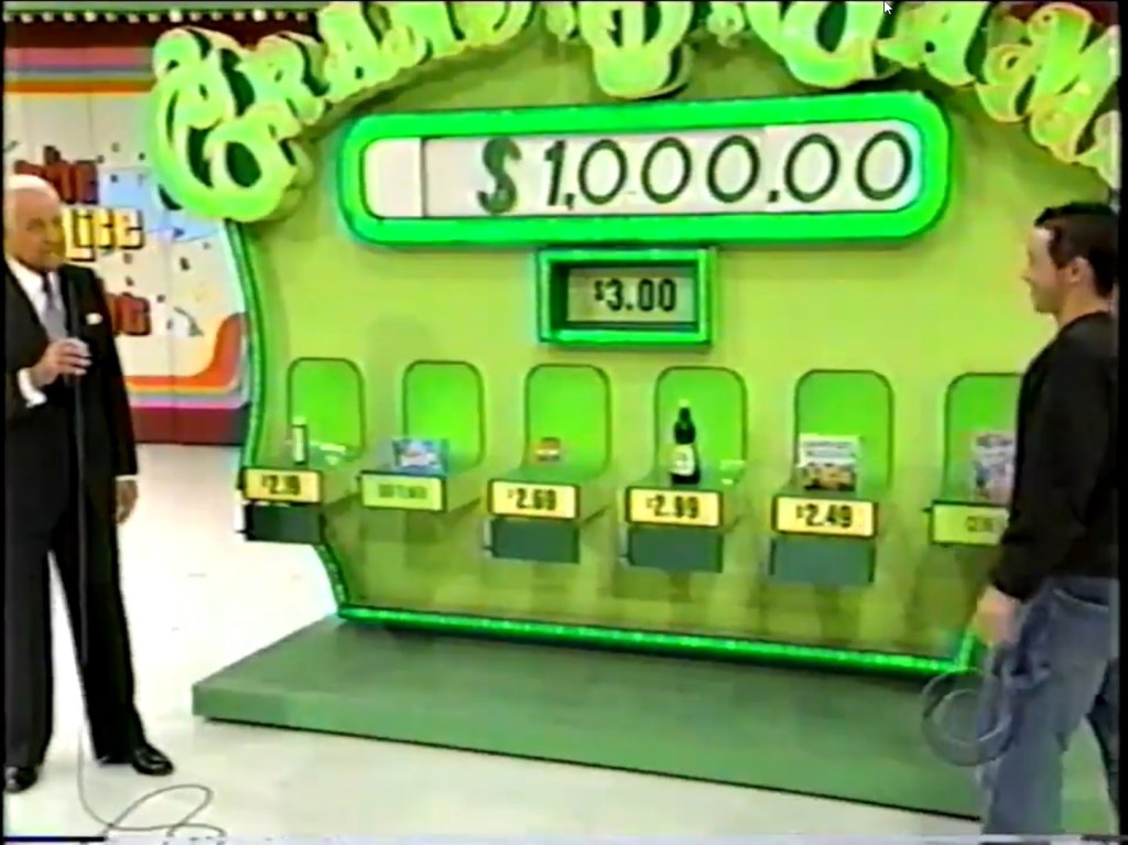 Contestant preparing to play the Grand Game on The Price is Right, with a display showing a cash prize of $1,000 and a target price of $3.00 surrounded by groceries with their prices.