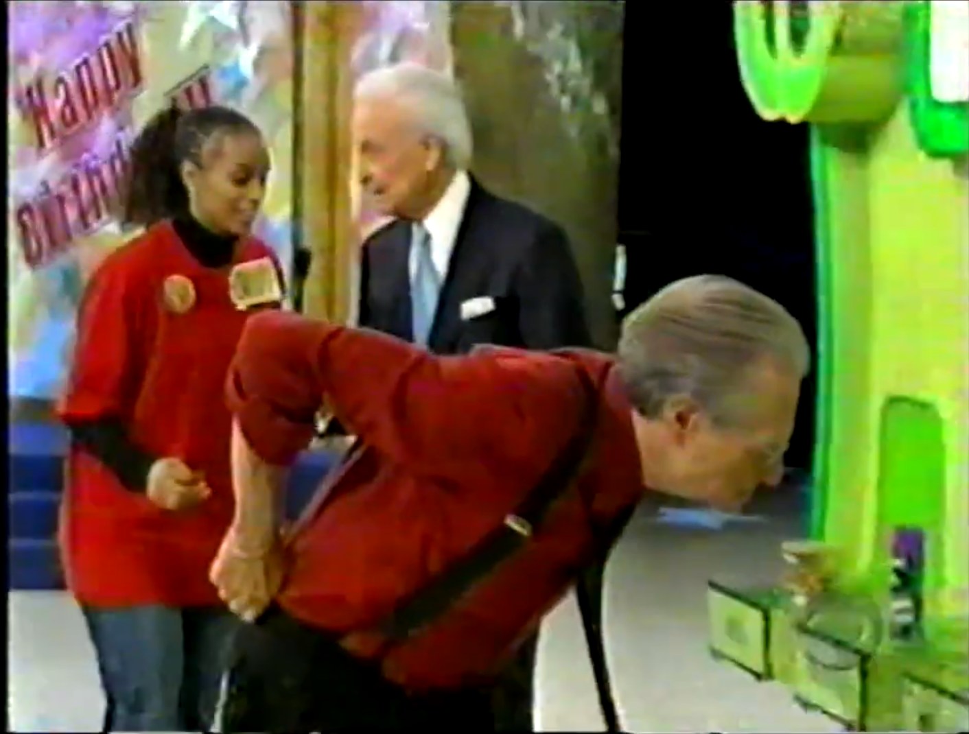 A contestant and host Bob Barker interact during the Grand Game on The Price is Right, with Larry King observing the product display.